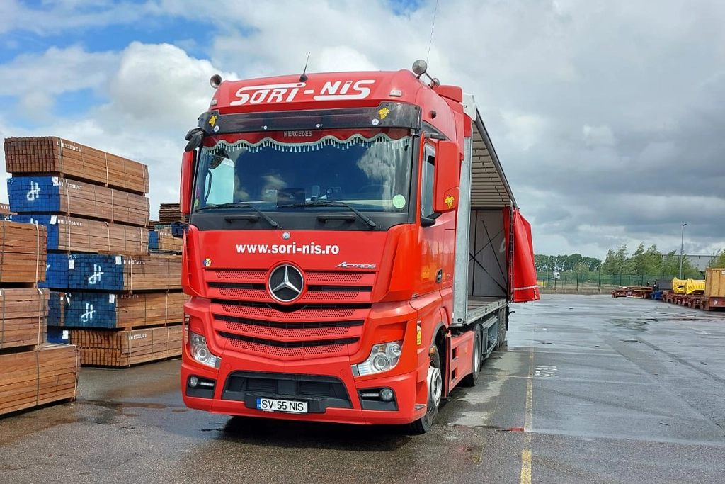 Camion Mercedes-Benz si semiremorca cu prelata desfacuta pe lateral pentru a fi incarcata cu marfuri